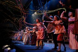 Colorful theatrical performance with actors throwing confetti and streamers in the air.