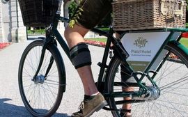 A man is riding a bicycle wearing traditional Bavarian Lederhosen.