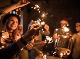Several guests at a Christmas party hold up lit sparklers.