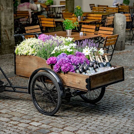 Ein mit Blumen geschmücktes "Platzl-Rad" steht bereit, um die Hochzeitsgäste mit kühlen Getränken zu empfangen.