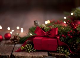 Rot eingepacktes Geschenk vor Tannenzweigen und weihnachtlicher Dekoration.