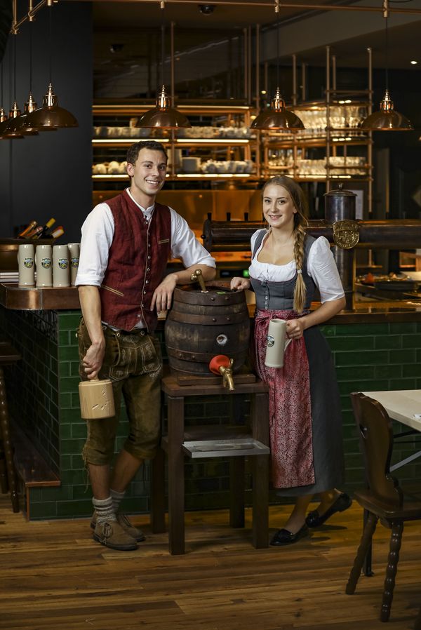 Zwei Mitarbeiter des Restaurants Ayinger in der Au in München stehen in Tracht an einem Bierfass angelehnt 