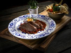 Pink roasted game with cranberry sauce is artfully arranged on porcelain plates.