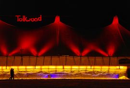 Tent at Tollwood Winter Festival at night, with two people strolling by.