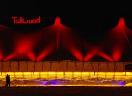 Tent at Tollwood Winter Festival at night, with two people strolling by.