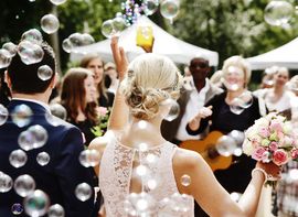 Hochzeitsgäste empfangen das Brautpaar, während die Braut einen bunten Brautstrauß in der Hand hält.